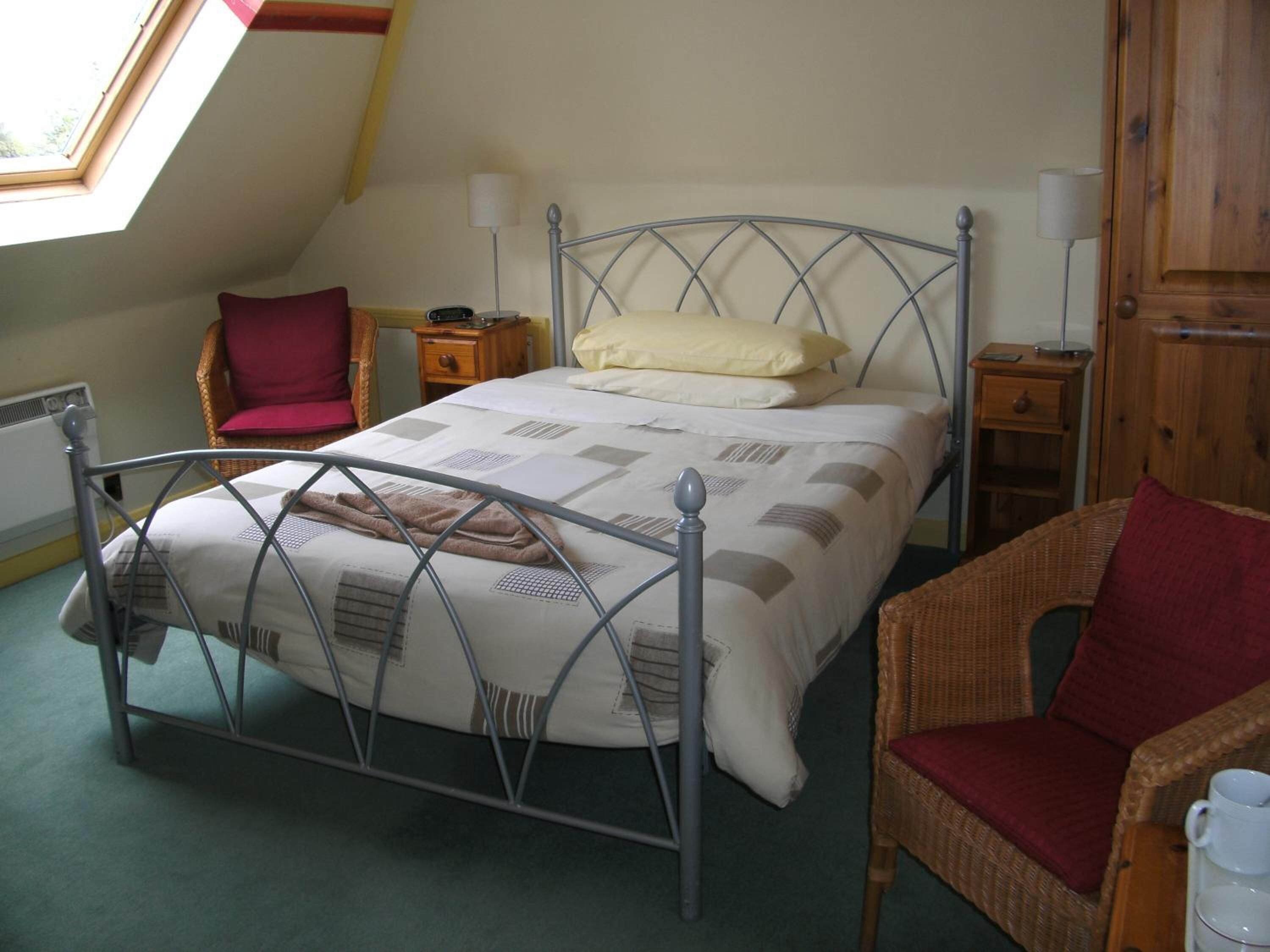 A bedroom with a metal bed frame, a red chair, a wooden nightstand, and a wooden wardrobe.