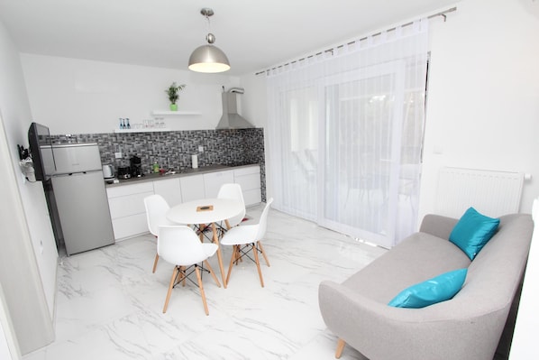 A modern kitchen with white cabinets, a built-in oven, and a dining area with a white table and chairs. - Apartment Karlo 1 (Rovinj)