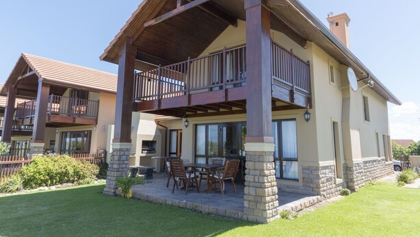 Une maison à deux étages dotée d’un patio couvert, de mobilier d’extérieur et de fondations en pierre.