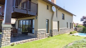 Une maison à deux étages avec un balcon, une terrasse dotée d’une table et de chaises, et une piscine.