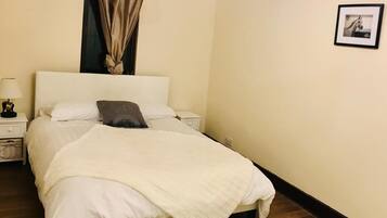 Un dormitorio con cama, mesita de noche, lámpara, lámpara colgante, un cuadro en la pared y suelo de madera.