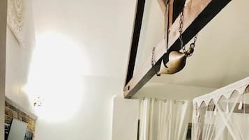 A bedroom with a wooden floor, a bed with a white canopy, a chest of drawers, a radiator, and a wall-mounted TV.