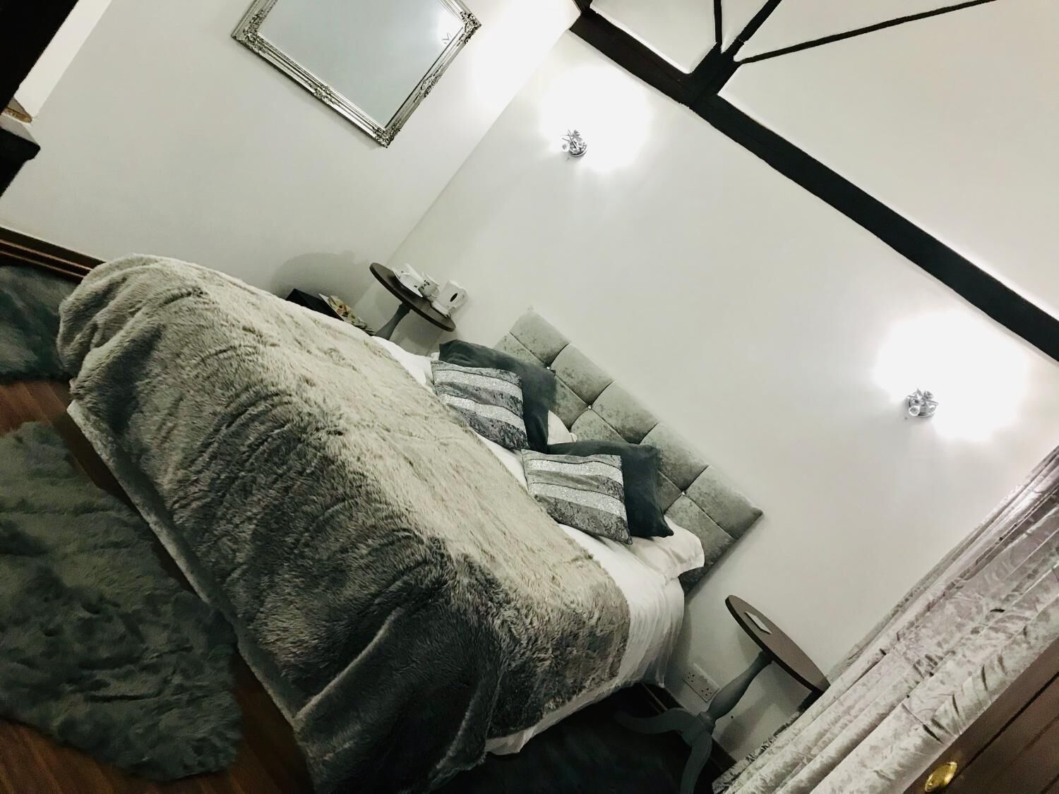 Een slaapkamer met een bed, nachtkastje, stoel, spiegel en raam met gordijnen.