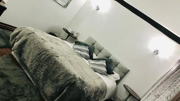 Een slaapkamer met een bed, nachtkastje, stoel, spiegel en raam met gordijnen.