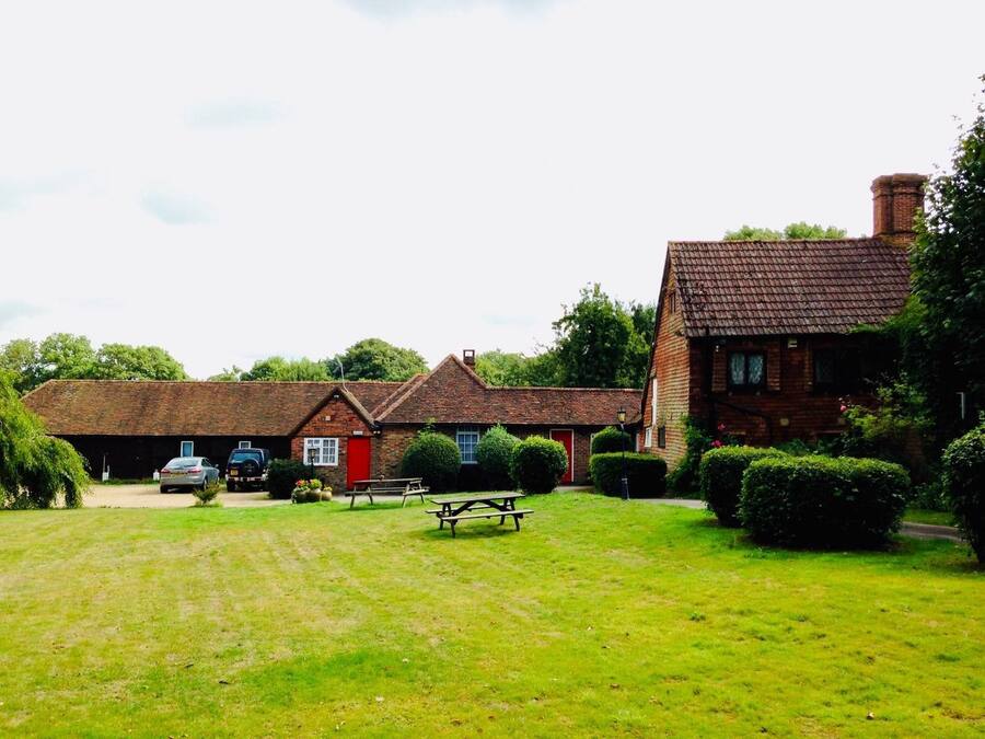 A rural setting with a large brick house, a red door, and a picnic table in the foreground.
