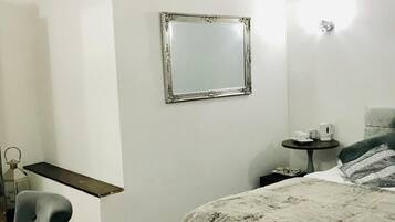 A bedroom with a bed, a chair, a small table with a lamp, and a mirror on the wall.
