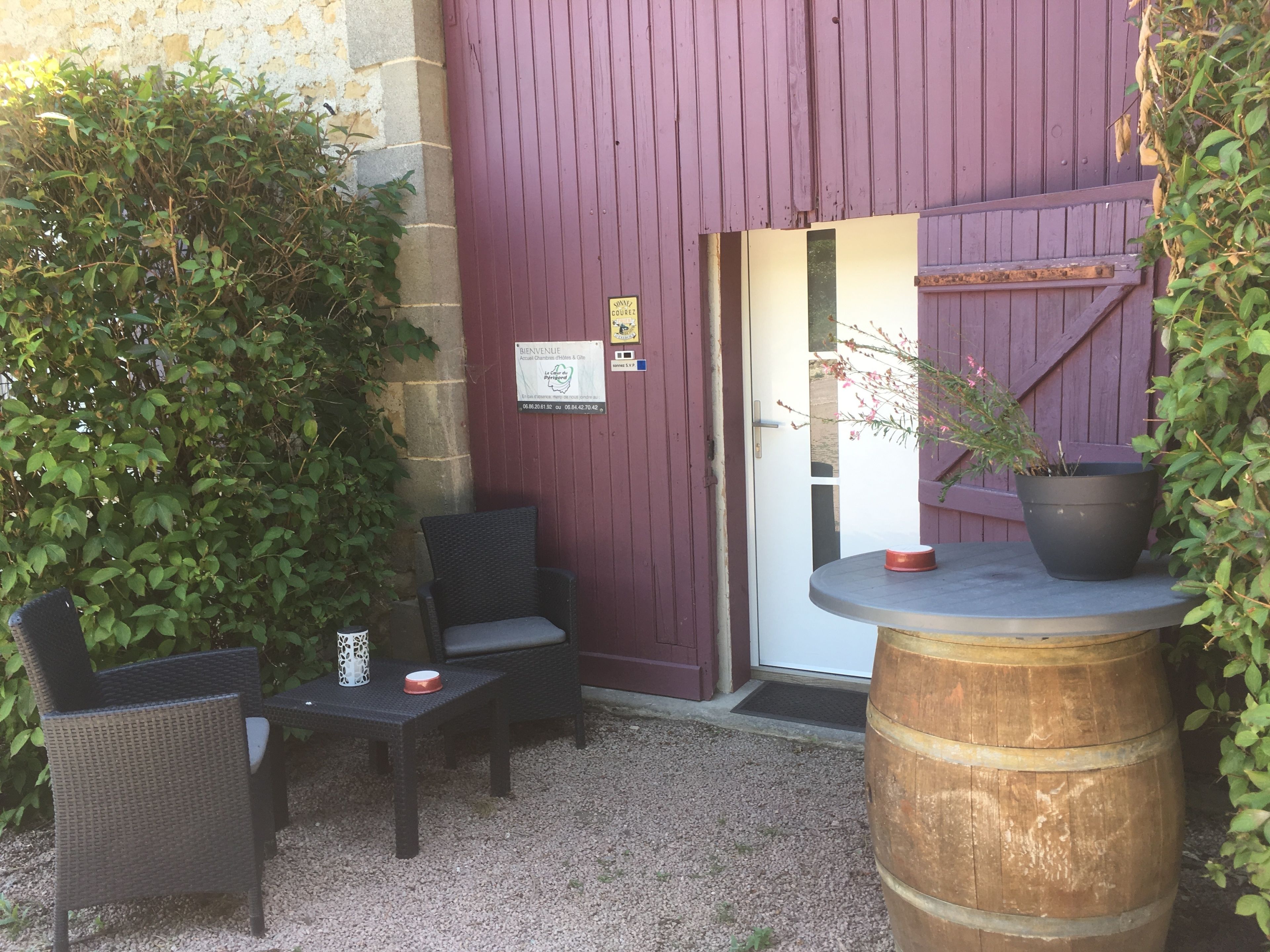 An outdoor seating area with wicker chairs and a table, a wooden barrel, and a potted plant.