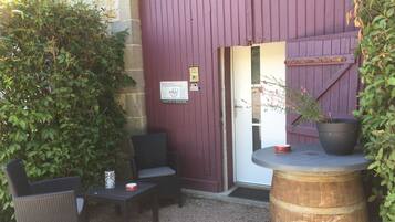 An outdoor seating area with wicker chairs and a table, a wooden barrel, and a potted plant.