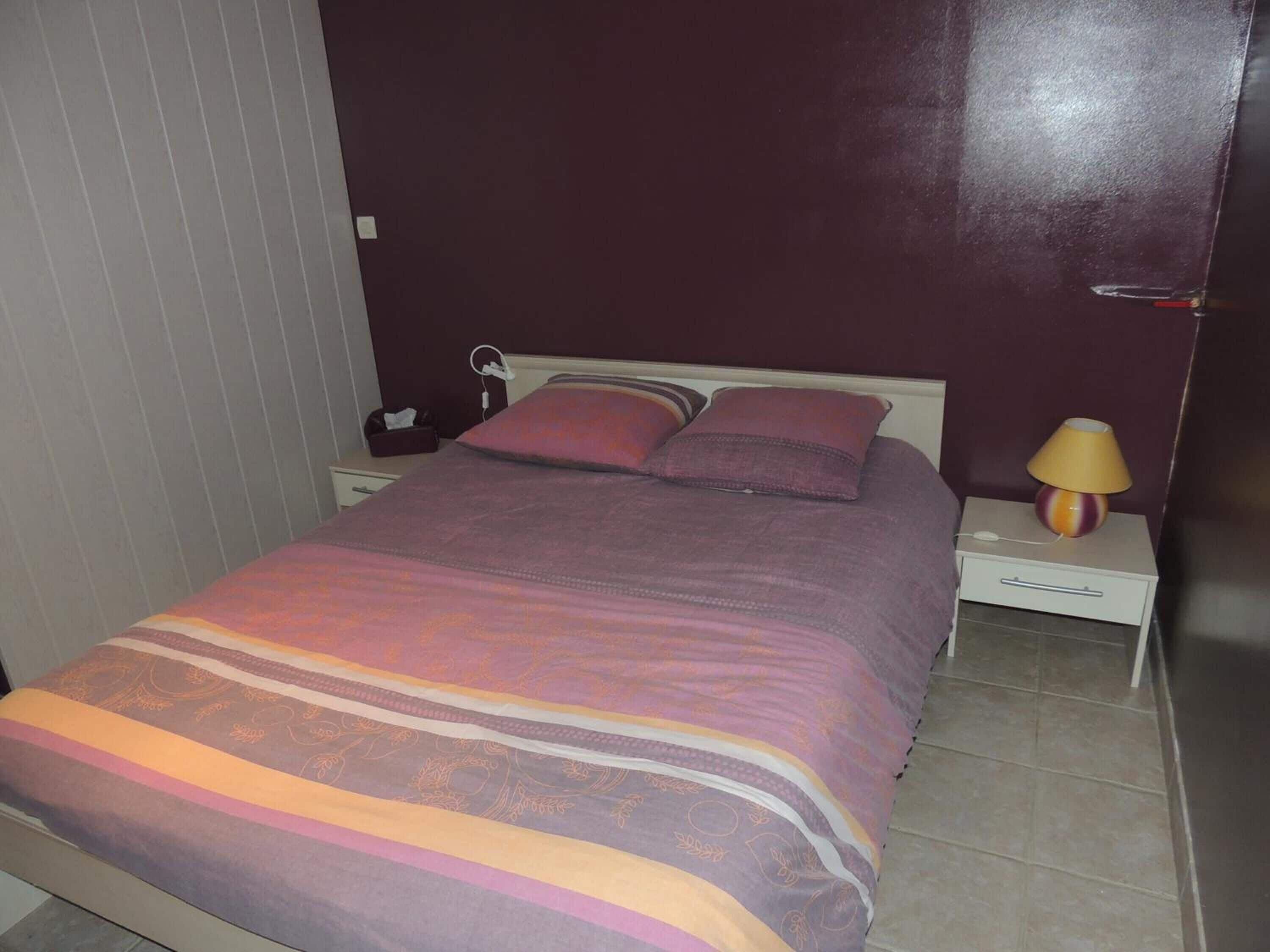 Une chambre à coucher avec un lit, des tables de chevet, une lampe et une prise électrique au mur.