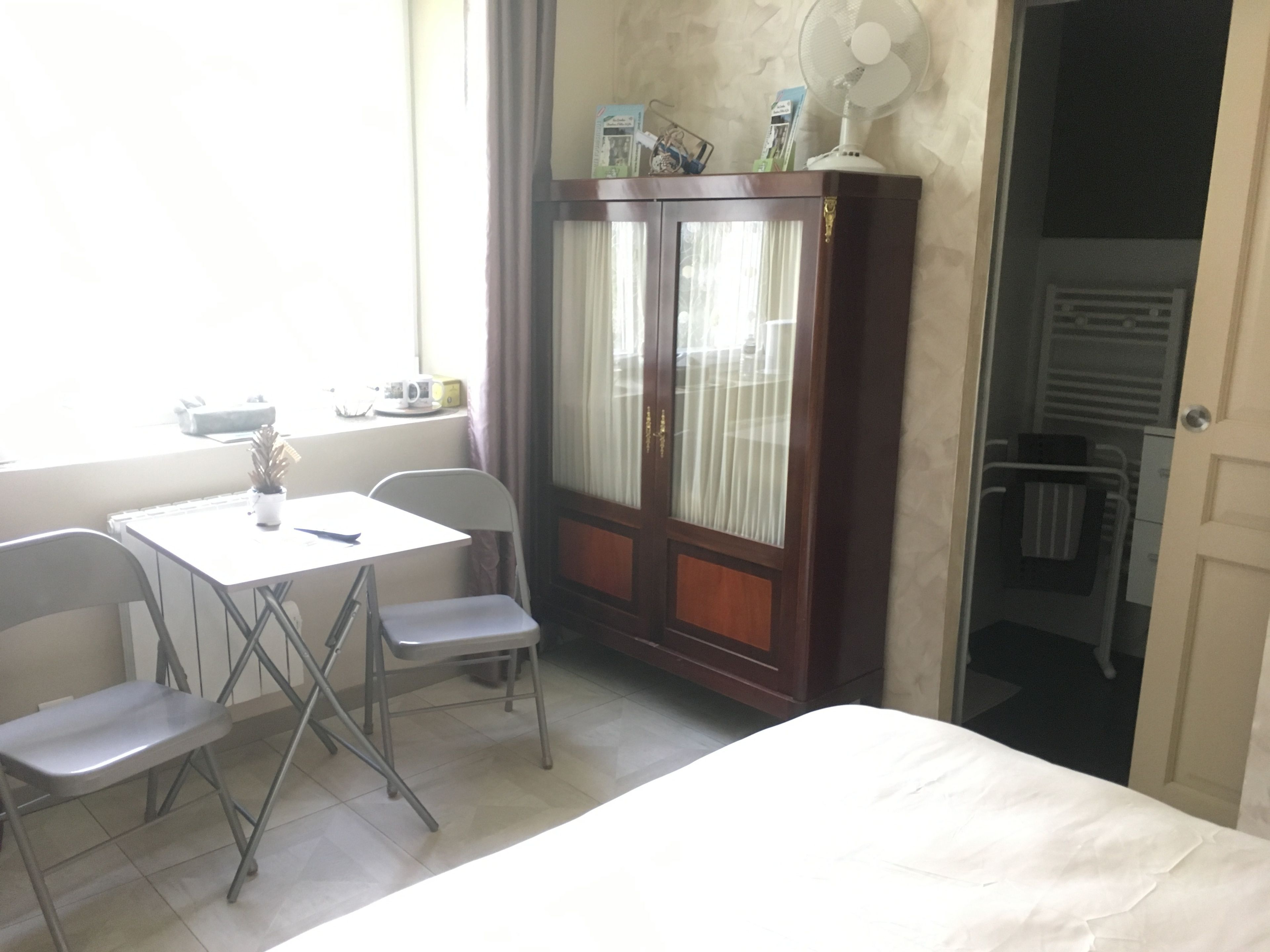 Ein Zimmer mit einem Bett, einem Tisch mit Stühlen, einem Schrank und einem Fenster mit Vorhängen.