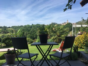 Un patio con dos sillas y una mesa, rodeado de plantas en macetas y vistas a una colina con una torre.