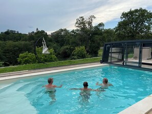 Una piscina con dos personas nadando, rodeada de follaje y un cielo despejado.
