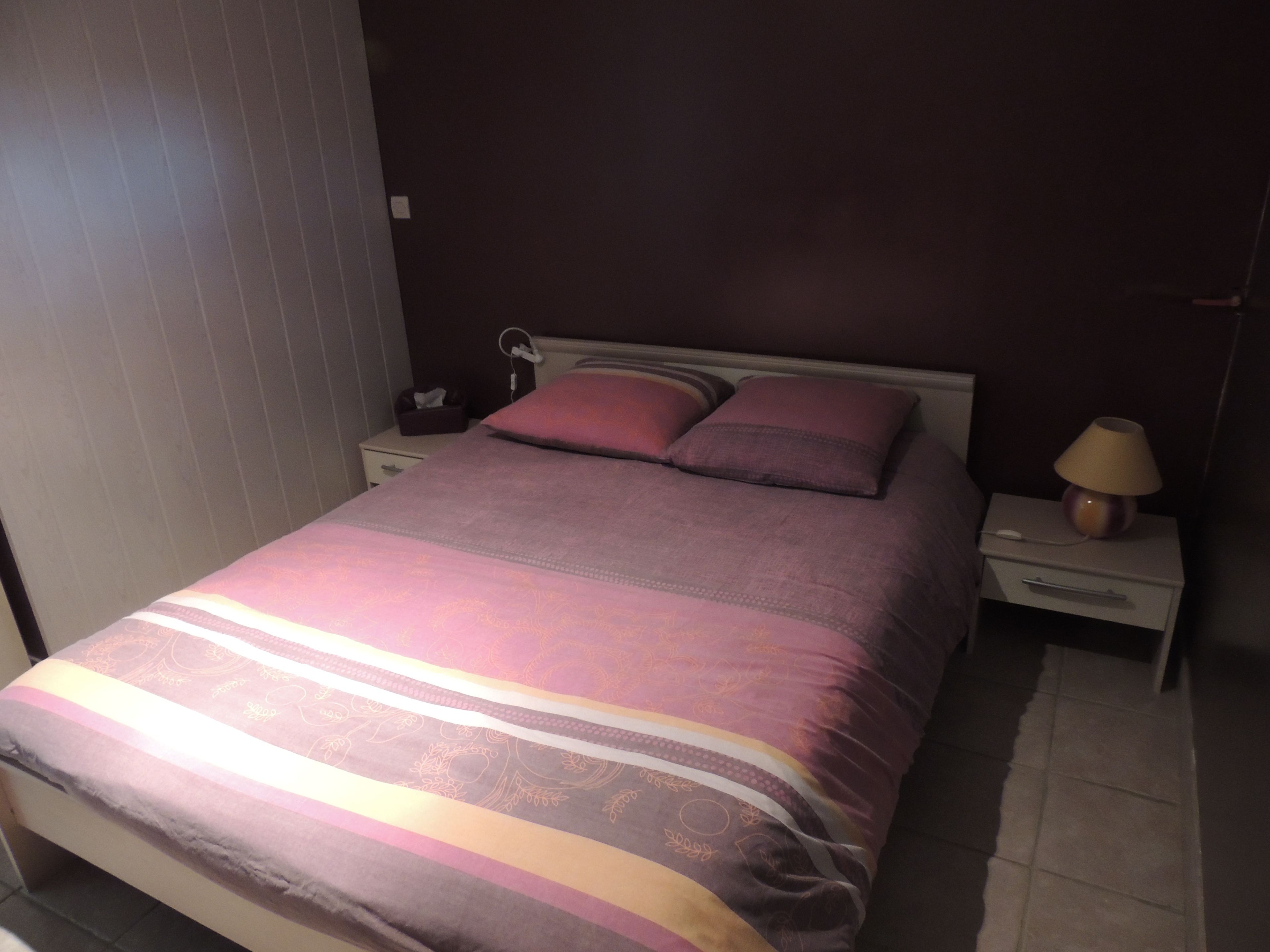 Una cama bien hecha con un edredón estampado, una mesita de noche con una lámpara y otra mesita con un teléfono y una caja de pañuelos.