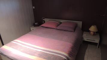 Una cama bien hecha con un edredón estampado, una mesita de noche con una lámpara y otra mesita con un teléfono y una caja de pañuelos.