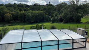 Una estructura tipo invernadero con una piscina debajo, rodeada de un jardín y árboles.