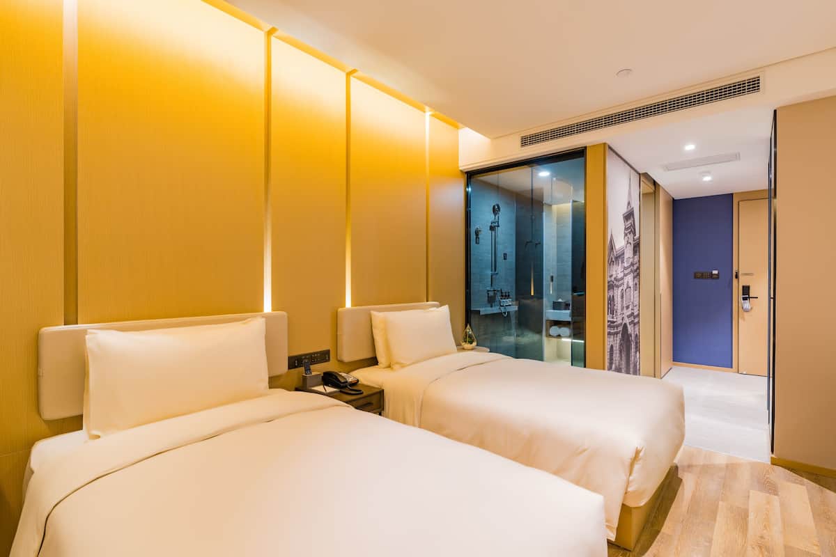 Ein Hotelzimmer mit zwei Betten, einer Duschkabine aus Glas und einem durch die Glaswand sichtbaren Badezimmer.