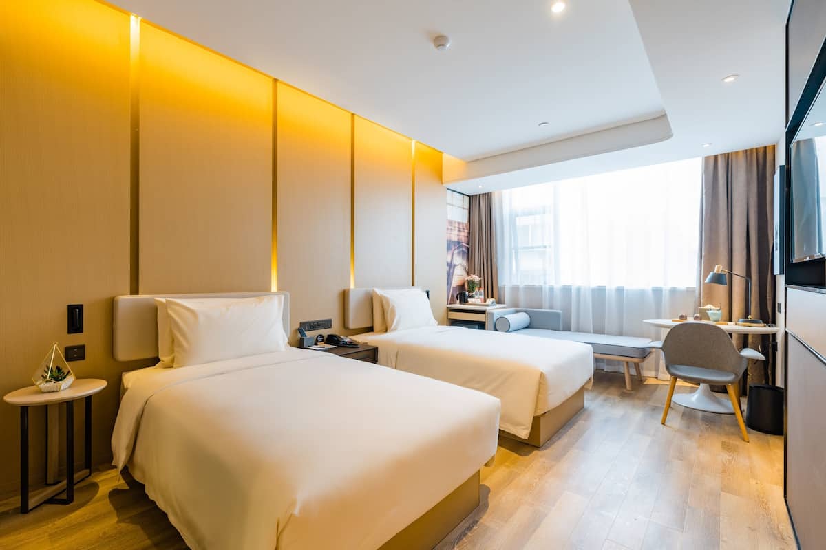 Ein Hotelzimmer mit zwei Betten, einem Schreibtisch, einem Stuhl, einem Fernseher und einem Fenster mit Vorhängen.