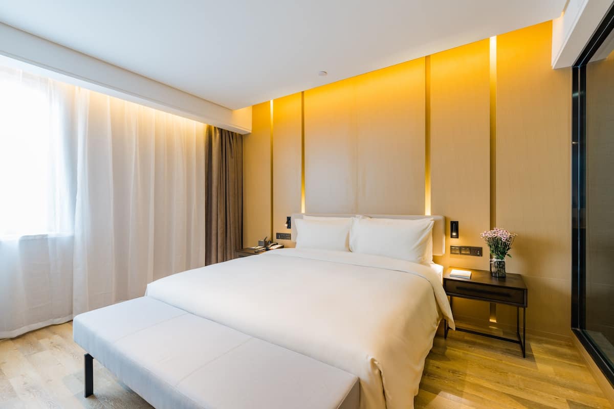 Ein modernes Hotelzimmer mit einem großen Bett, Nachttischen und einem Fenster mit Vorhängen.