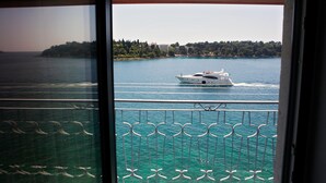 A balcony with a view of a body of water, a yacht, and a distant shoreline with buildings and trees.