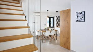 A modern interior with a wooden staircase, a dining area with a white table and chairs, and a geometric wall pattern.