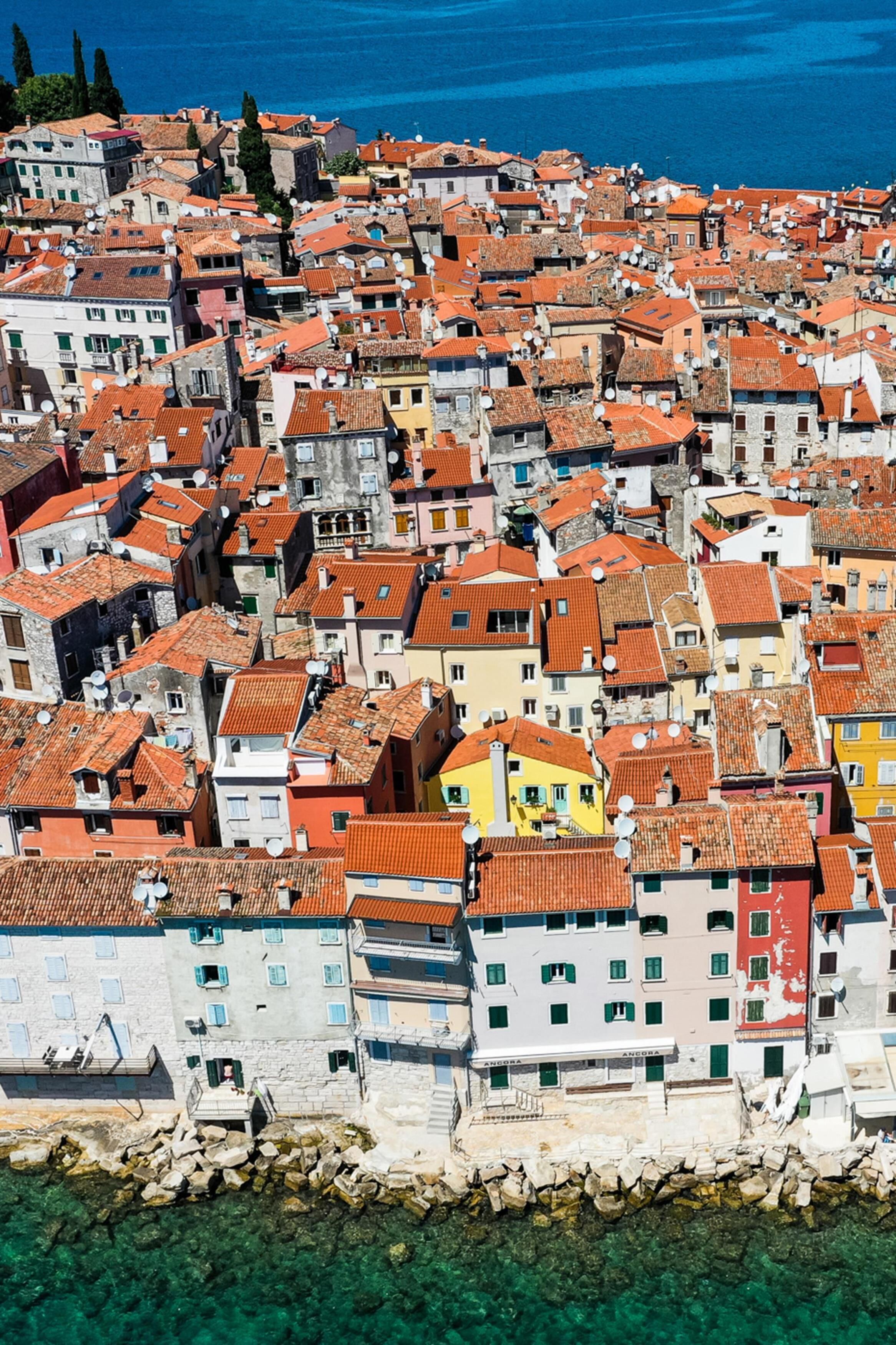 A coastal town with tightly packed buildings, clear blue sea, and rocky shoreline.