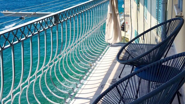 A balcony with a view of the sea, featuring a chair and a railing.