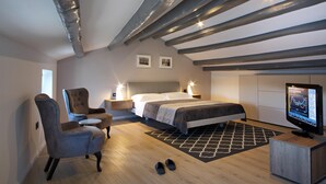 A modern bedroom with a bed, two chairs, a TV, and a wooden floor.