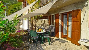 A patio with a table and chairs, a wooden door, and a stone wall. - Holideal Casa Paola (Tremosine)