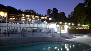 A swimming pool area with a white fence, steps leading to a deck, and a building with lights in the background.