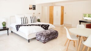 A modern bedroom with a large bed, bedside tables, a dining area with chairs, and a wardrobe.