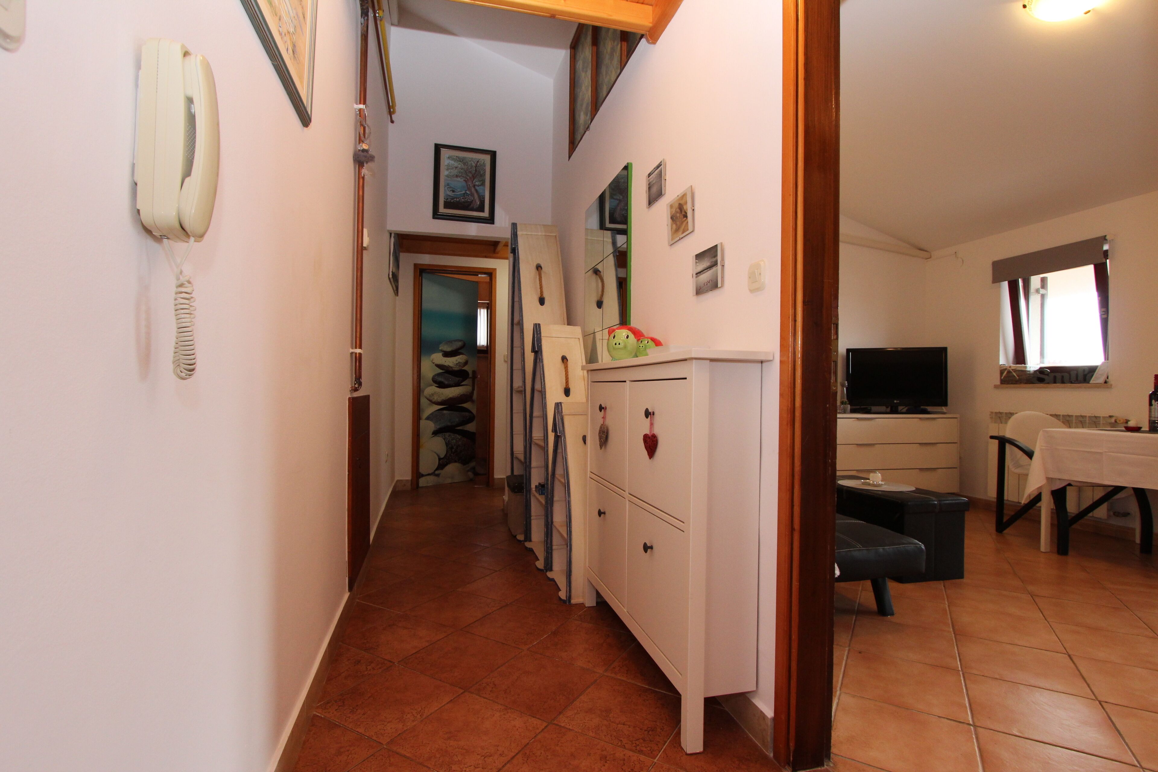 A narrow hallway with a telephone, a mirror, and a staircase leading to another room.