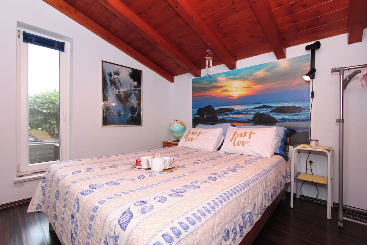 Une chambre à coucher avec un lit, une table de chevet, un globe terrestre et un tableau représentant un coucher de soleil sur l’océan.