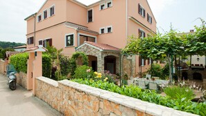 A two-story house with a stone wall in front, a parked scooter, and a garden with various plants and flowers. - Apartments Villa Nikola (Rovinj)