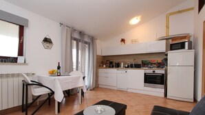 A compact kitchen with white cabinets, a microwave, and an oven. There's a dining table with chairs and a small table with a bottle and glasses. - Apartments Villa Nikola (Rovinj)