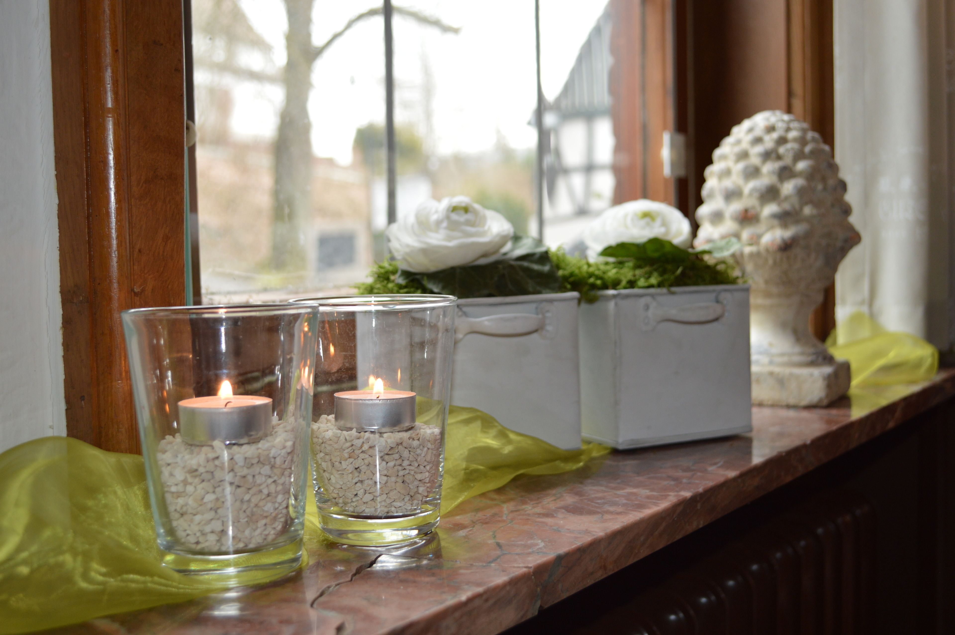 Two glass candle holders with candles on a window sill, surrounded by decorative items.