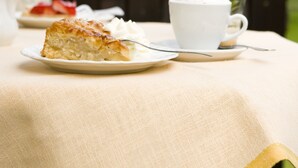 Een tafel met een stuk taart en een kop koffie op een tafelkleed, met een tuin op de achtergrond.