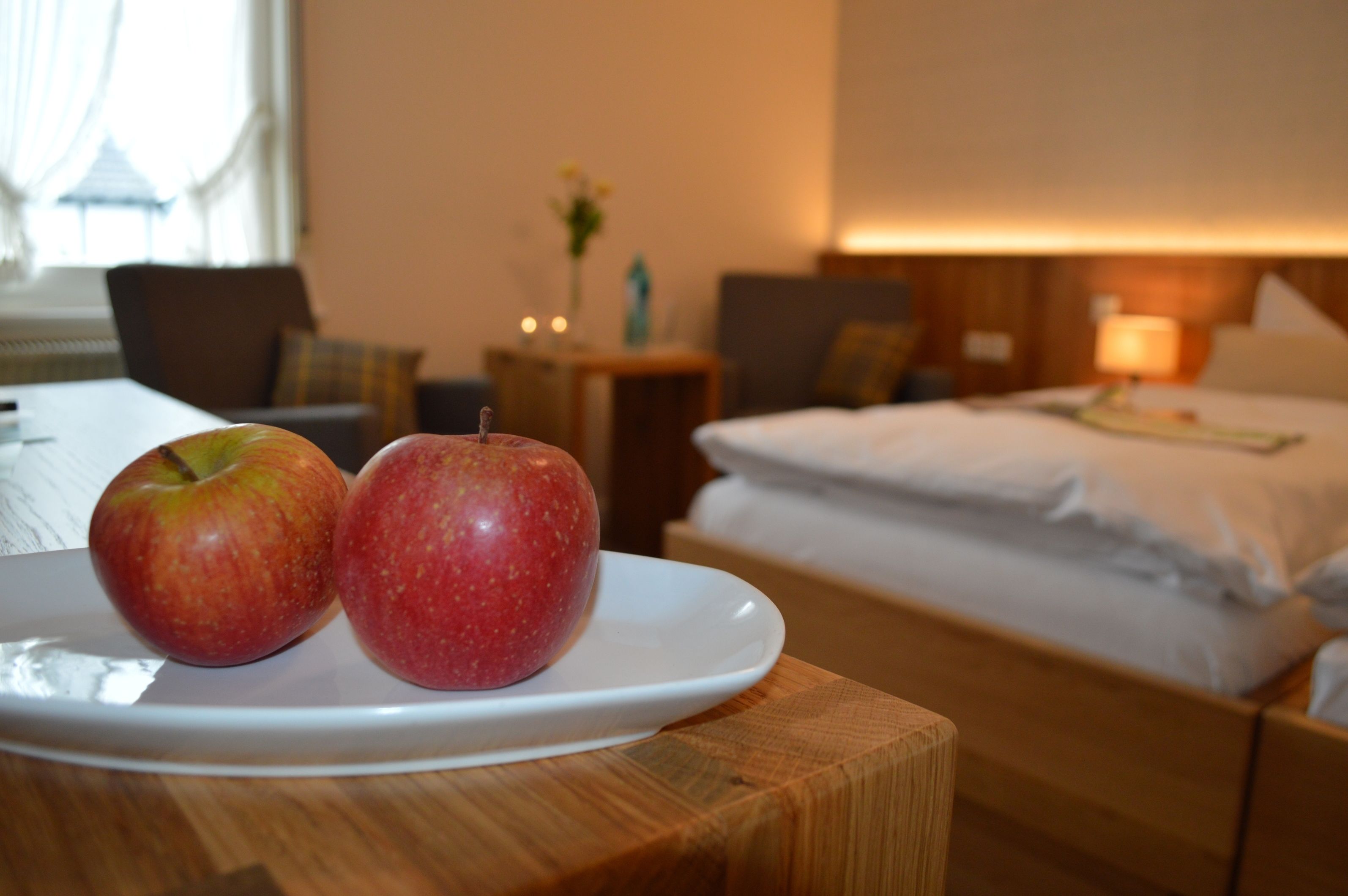 Ein Hotelzimmer mit Bett, Nachttisch und einem Teller mit zwei Äpfeln auf einem Holztisch.