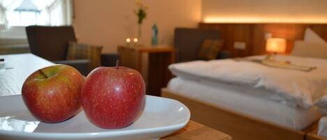 Una habitación de hotel con una cama, mesita de noche y un plato con dos manzanas sobre una mesa de madera.