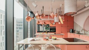 A modern kitchen with a large island, hanging copper pots, and a view of the city through large windows. - lyf East Frankfurt (Frankfurt)