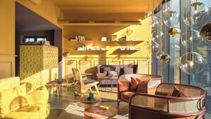 A modern living room with yellow walls, a bookshelf, and a large window with a city view. - lyf East Frankfurt (Frankfurt)