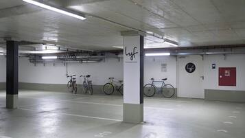A parking garage with concrete pillars, fluorescent lighting, and bicycles parked against the walls.