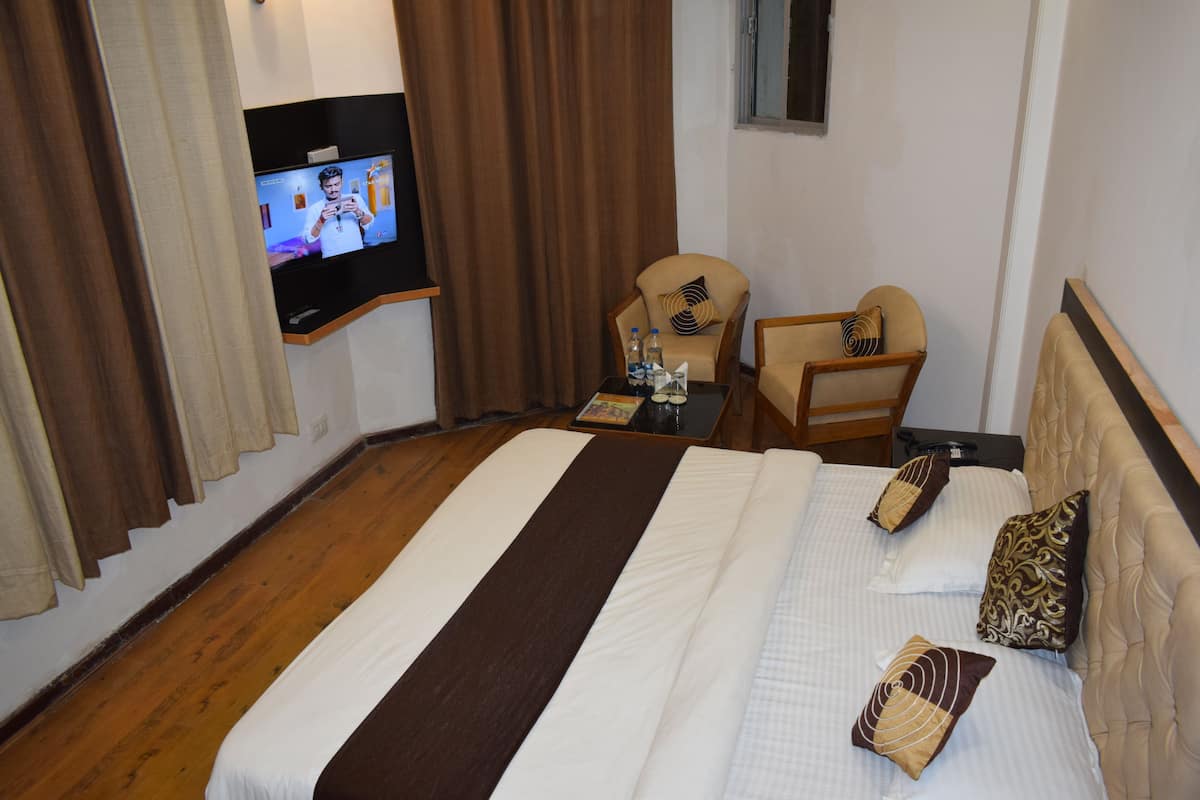 A hotel room with a large bed, two armchairs, a small table with a remote control, and a TV mounted on the wall.