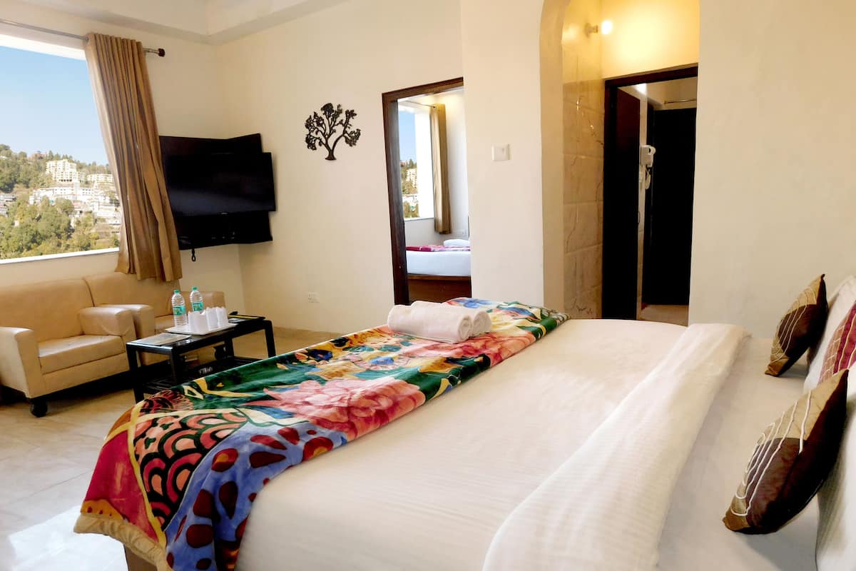 A hotel room with a bed, a sofa, a TV, and a bathroom visible through an open door.