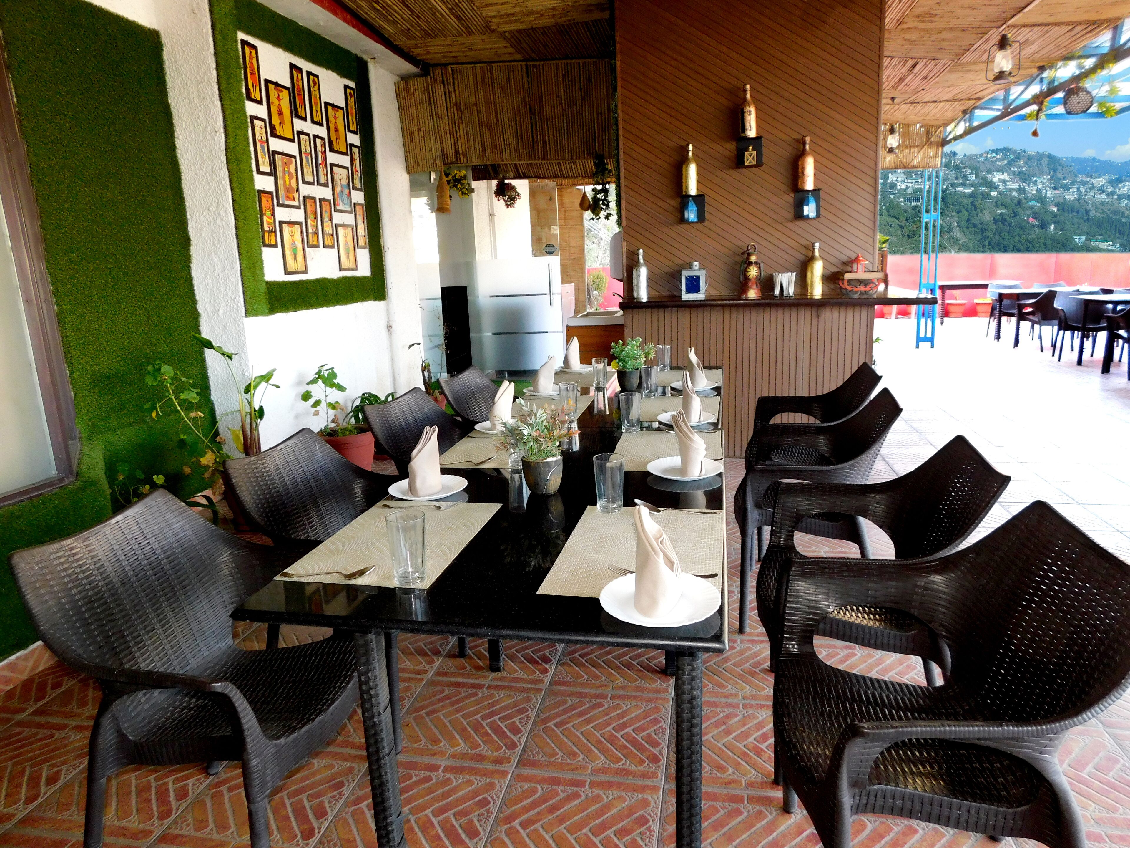 Un restaurant avec des tables et des chaises noires, des murs verts et une vue sur la ville.