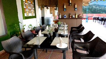 Um restaurante com mesas e cadeiras pretas, paredes verdes e vista para a cidade.