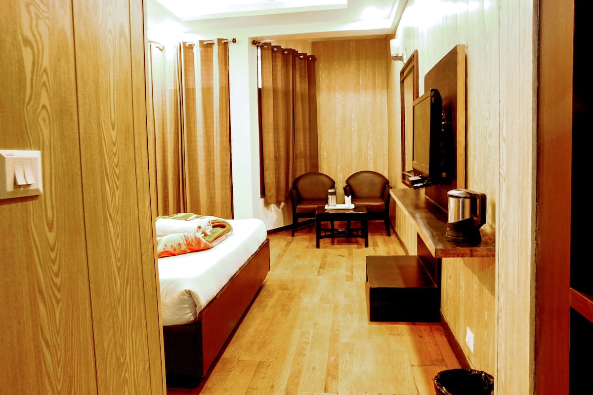 A hotel room with a bed, a desk, two chairs, a television, and a ceiling fan.