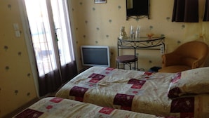 A bedroom with two beds, a small table with a chair, a television, and a window with curtains. - Chambre d'hôtes Fabilio (Marseille)