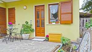 A yellow building with a wooden door, a window with a curtain, and a small table with chairs. - Holideal Casa Rosalia (Tremosine)
