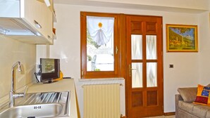 A compact kitchen with a sink, a small television, and a radiator. There's a wooden door with a window, and a painting on the wall. - Holideal Casa Rosalia (Tremosine)