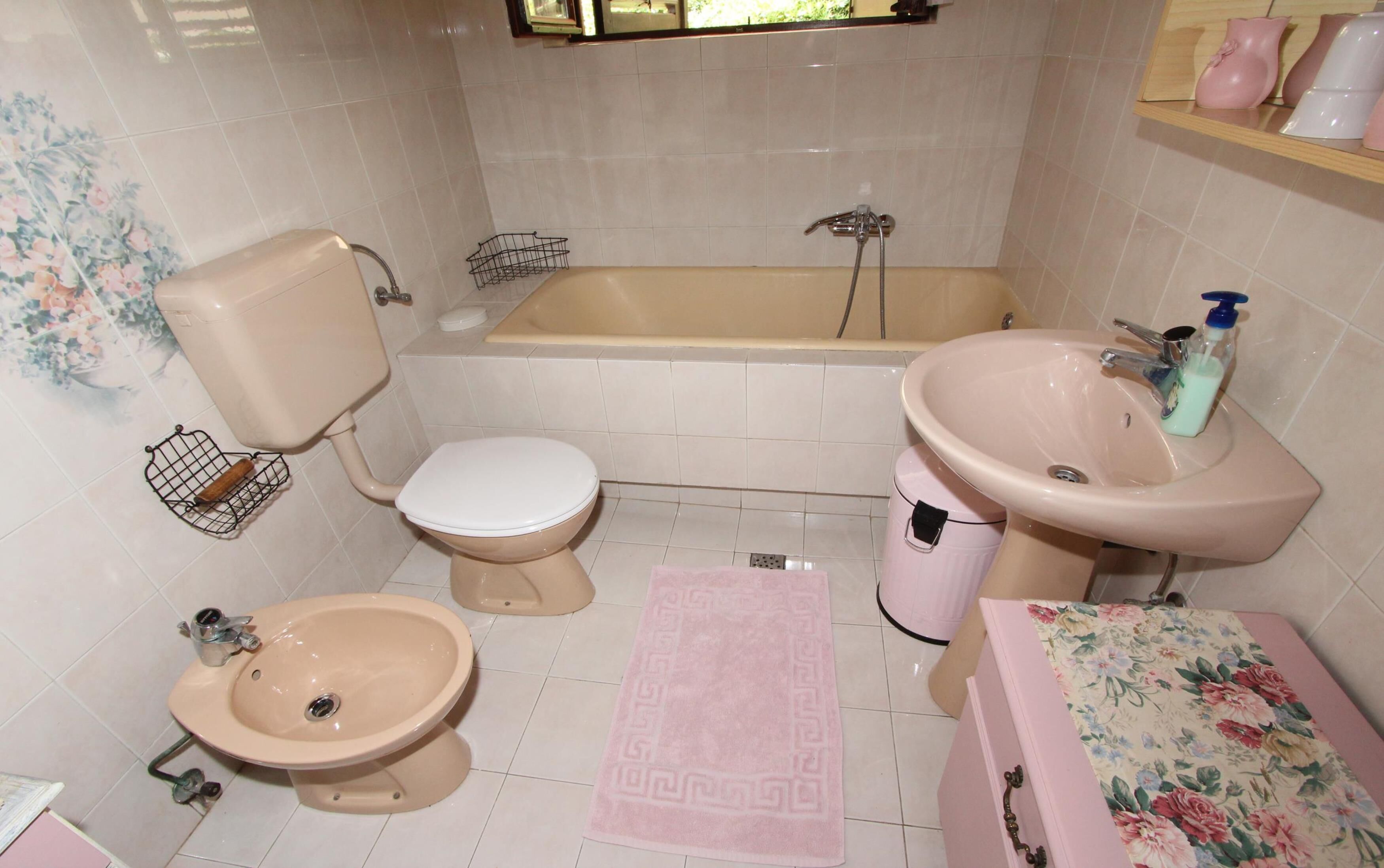 A bathroom with a toilet, bidet, bathtub, sink, and a small rug.
